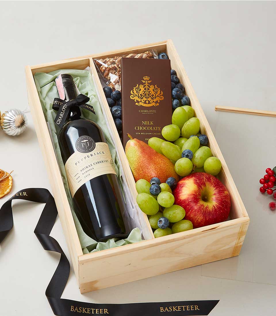 A luxurious wooden gift box, showcasing an exquisite ensemble: a bottle of fine red wine, a decadent chocolate bar, and an array of fresh fruits including succulent grapes, vibrant blueberries, a crisp apple, and a juicy pear. The contents are elegantly nestled within layers of white and green tissue paper. To complete the sophisticated presentation, a black ribbon adorned with the 