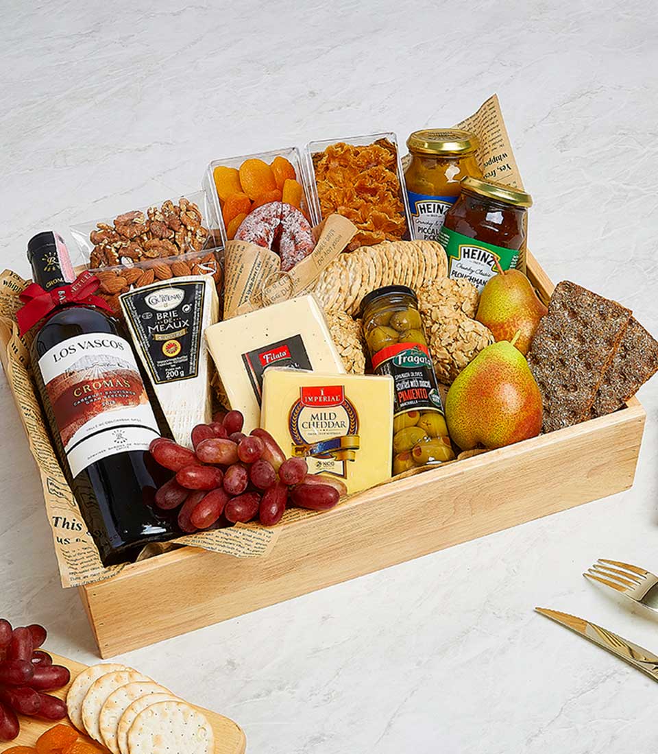 A luxurious gourmet wine and cheese gift box from Basketeer beautifully presents a bottle of exquisite red wine, an assortment of premium cheeses, savory crackers, gourmet olives, succulent dried fruits, artisanal nuts, and two perfectly ripe pears. The opulent arrangement includes delightful touches such as a jar of golden honey and sleek cheese spreader, all nestled in an elegant box adorned with the distinguished Basketeer logo. Finishing the lavish display is a charming corkscrew fork—every detail meticulously curated to create an inviting and indulgent experience.