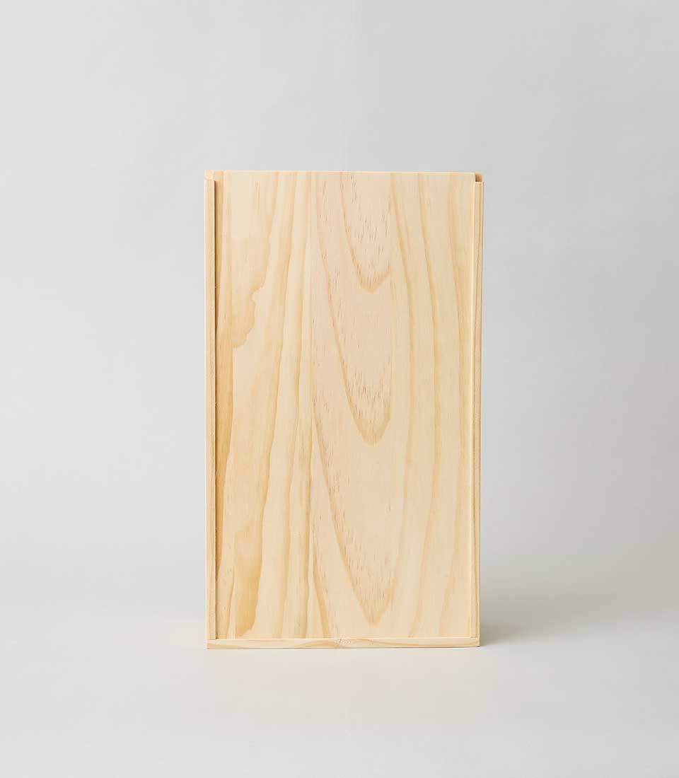 A beautifully crafted, rectangular wooden box from Basketeer stands elegantly upright against a soft, light grey backdrop. The luxurious light-colored wood features a smooth finish adorned with natural wood grain patterns, embodying sophistication and refinement. A stately ribbon emblazoned with the Basketeer logo drapes gracefully across the surface, hinting at the exquisite contents within. This exquisite piece exudes an aura of timeless elegance and invite-only exclusivity.