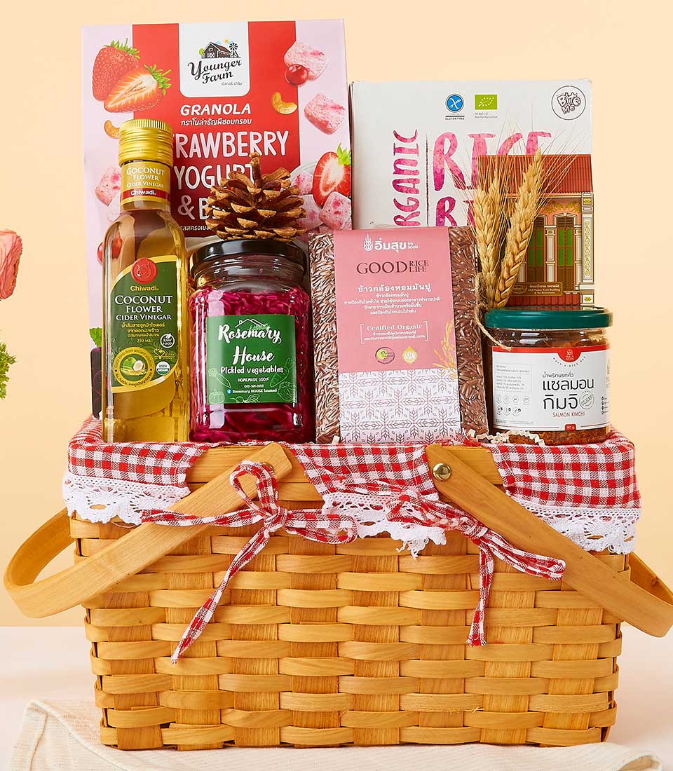 A beautifully crafted wicker basket, draped elegantly in a luxurious Basketeer red and white gingham cloth, presents an inviting array of gourmet delights. This exquisite hamper features Basketeer's signature ribbon and logo, showcasing an assortment of premium treats including velvety strawberry yogurt granola, nutrient-rich rice berry, pure coconut cooking oil, artisanal jam in a glass jar, an indulgent handmade soap bar, a freshly baked loaf of bread, and a savory jar of sauce. A perfect embodiment of Basketeer's dedication to quality and elegance.
