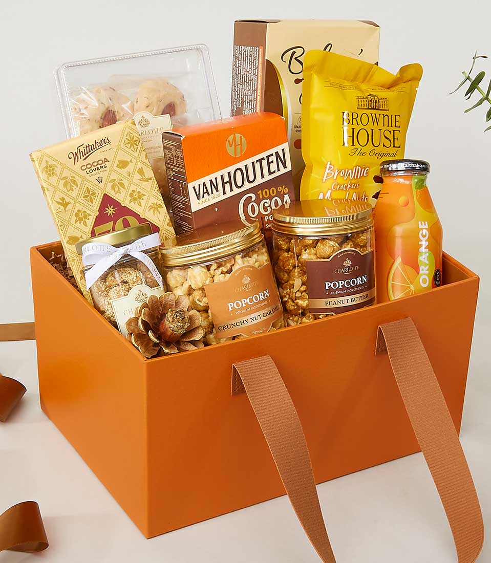 A luxurious orange gift box from Basketeer brimming with an exquisite assortment of gourmet treats. Nestled inside are two elegant jars of premium popcorn, a sophisticated bottle of freshly squeezed orange juice, a decadent packet of Van Houten cocoa, and an opulent box of artisan cookies. The experience continues with a luscious package of rich brownie brittle, a refined pack of assorted chocolates, and an elegant small box of savory cheese crispies. Each item is carefully curated to create a lavish and inviting scene that embodies the thoughtful luxury that Basketeer promises.