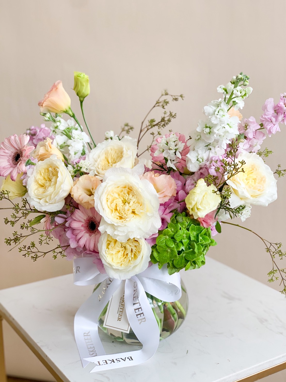 Elegant pastel garden flower vase arrangement with white roses, pink gerberas, and seasonal blooms.
