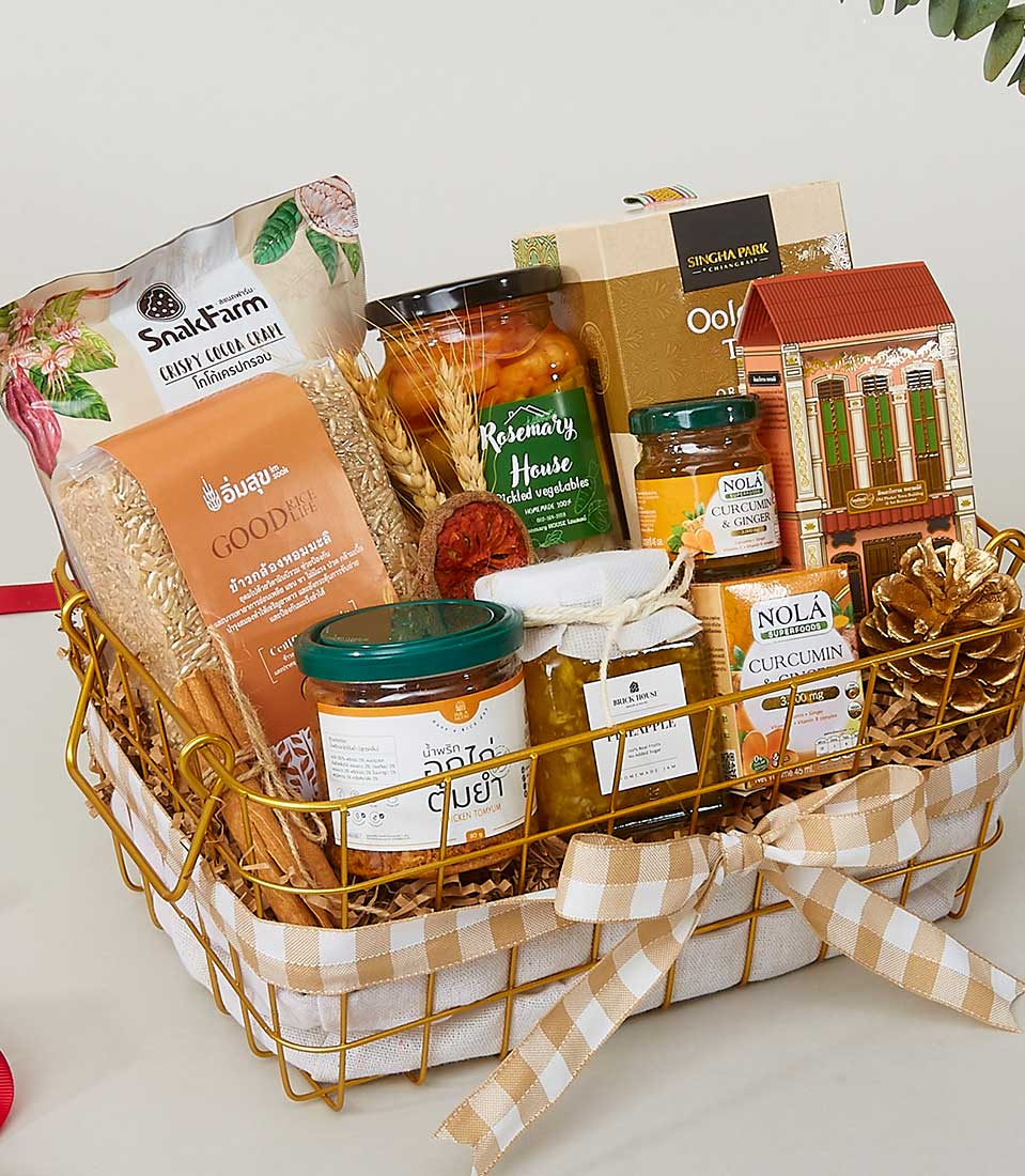 A luxurious Basketeer gift basket brimming with an exquisite selection of gourmet delights, including premium oat flakes, artisanal pickles, golden honey, a rich turmeric blend, and a variety of herbal supplements. This opulent gold-colored basket features an elegant beige and white checkered bow adorned with the distinguished Basketeer logo. Artfully arranged on a pristine white surface, it invites indulgence and sophistication at every glance.