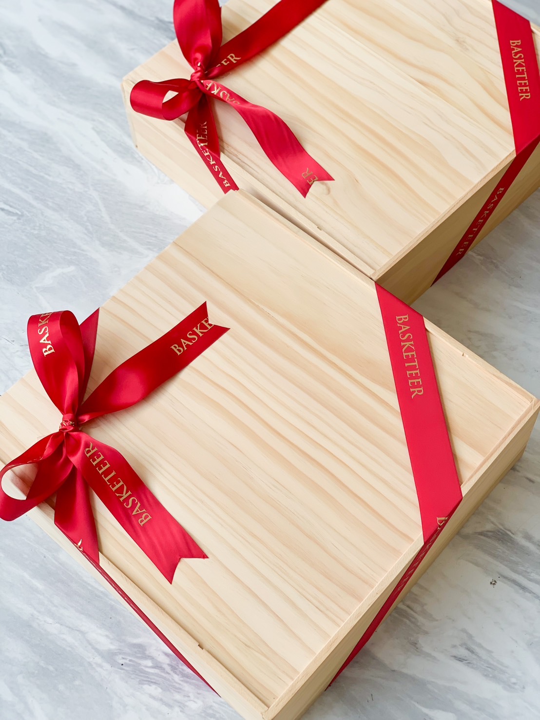 Two light wooden gift boxes, tied with red ribbons imprinted with the word 