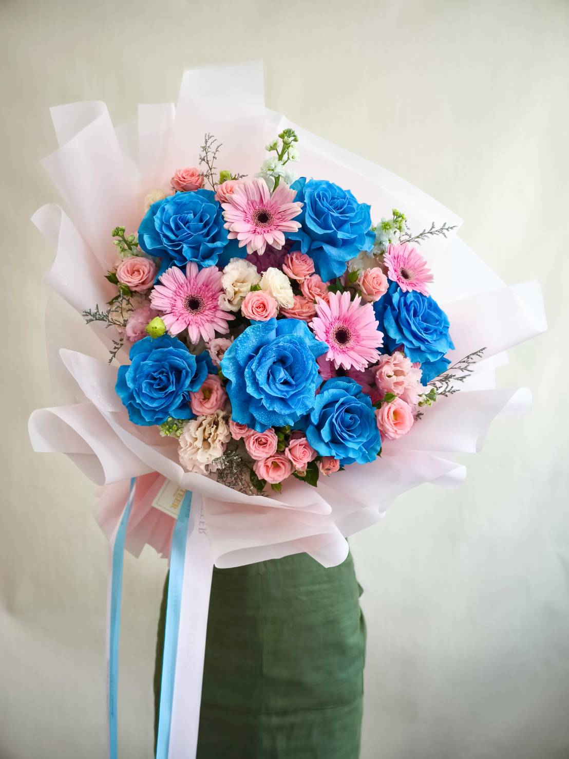 Elegant bouquet with blue roses, pink gerberas, spray roses, and soft pastel flowers, wrapped in pink paper.