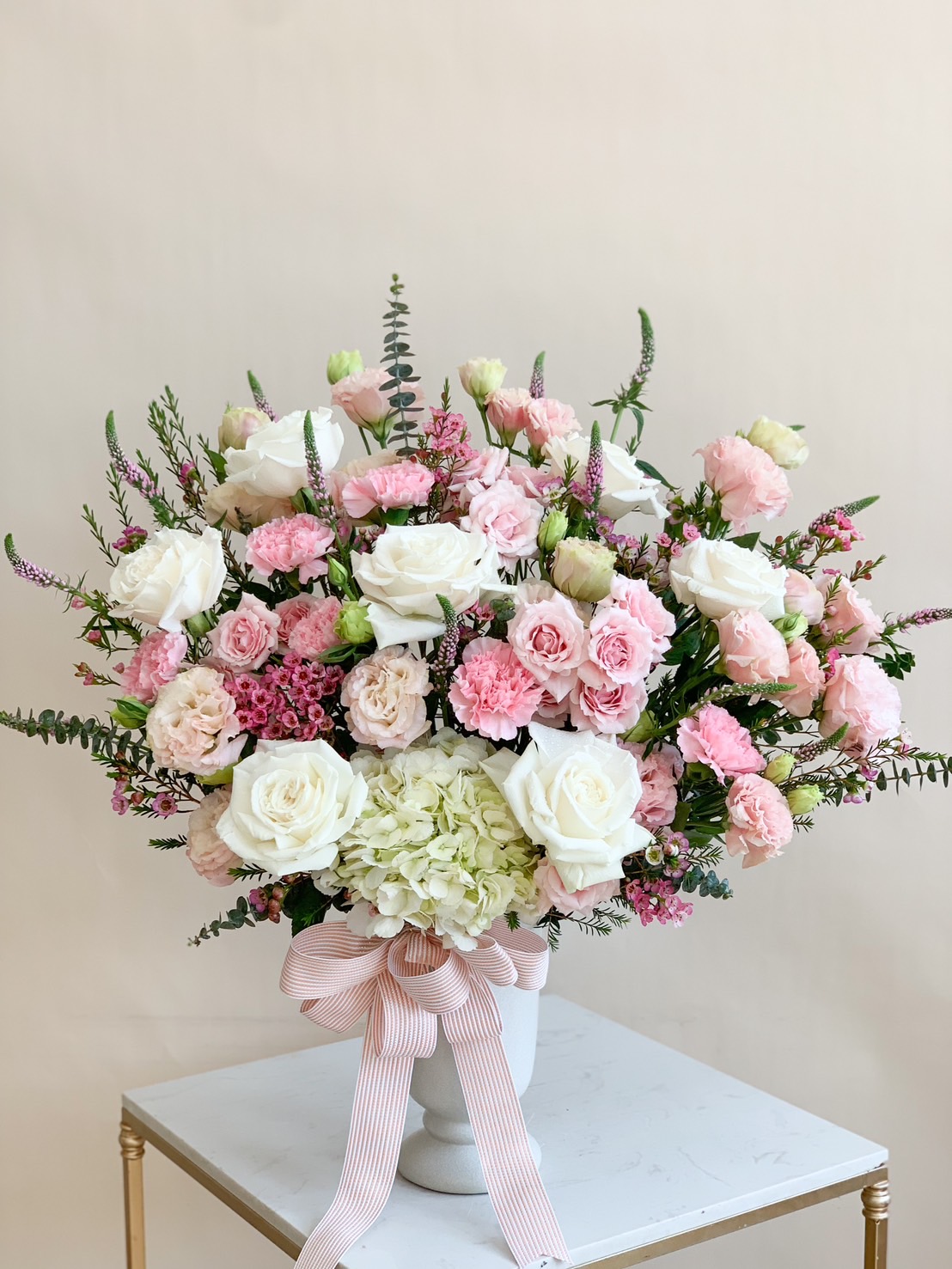 Blush pink and white luxury flower arrangement in an elegant vase with a soft pink ribbon.