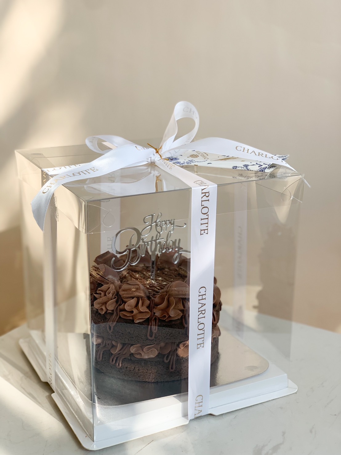 Delight in Charlotte Bakery’s chocolate birthday cake, elegantly boxed with signature ribbon and decorative topper, crafted in Bangkok.