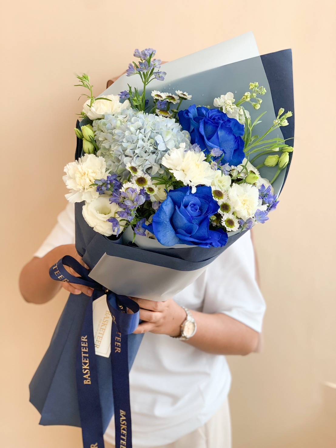 A luxurious bouquet featuring a royal blue rose, blue hydrangeas, and white flowers, wrapped in navy blue paper with a matching ribbon.