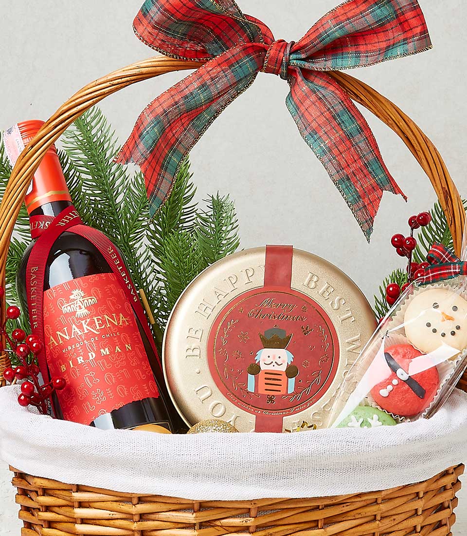 A sumptuous wicker basket adorned with an elegant red and green plaid bow captures your attention instantly. Nestled within is a distinguished bottle of Anakena red wine, ready to enhance any celebration. Accompanying this exquisite wine is a radiant golden tin, elegantly inscribed with 