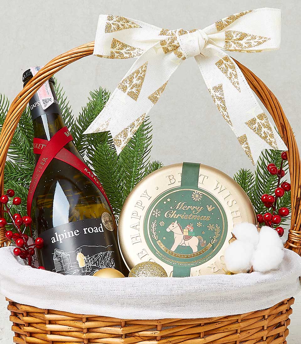 A luxurious Basketeer festive gift basket, tastefully arranged with a bottle of exquisite Alpine Road wine and a charming Merry Christmas tin. Nestled within, a ceramic plate inscribed with 