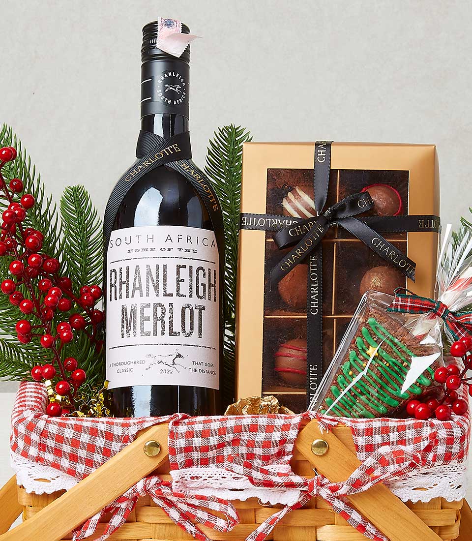 An opulent holiday gift basket that exudes elegance and warmth, featuring a refined bottle of Rhanleigh Merlot nestled amidst a delightful assortment of luxurious chocolates. A festive candy cane adds a touch of whimsical charm, while sprigs of holly and pine evoke the spirit of the season. The basket is beautifully adorned with rich red ribbons and lined with a stylish checkered cloth. Adding to its allure, elements such as ribbons or boxes prominently display the illustrious Basketeer logo, ensuring this exquisite gift is both memorable and inviting.