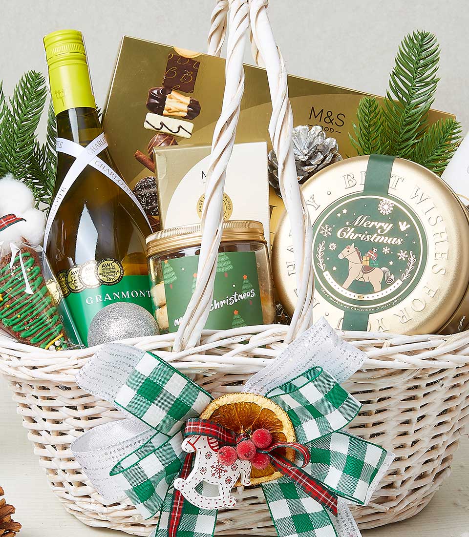 The image showcases an exquisite Basketeer festive gift basket, brimming with holiday-themed delights. It features a sophisticated bottle of white wine, a selection of indulgent chocolates, and a charming jar labeled 