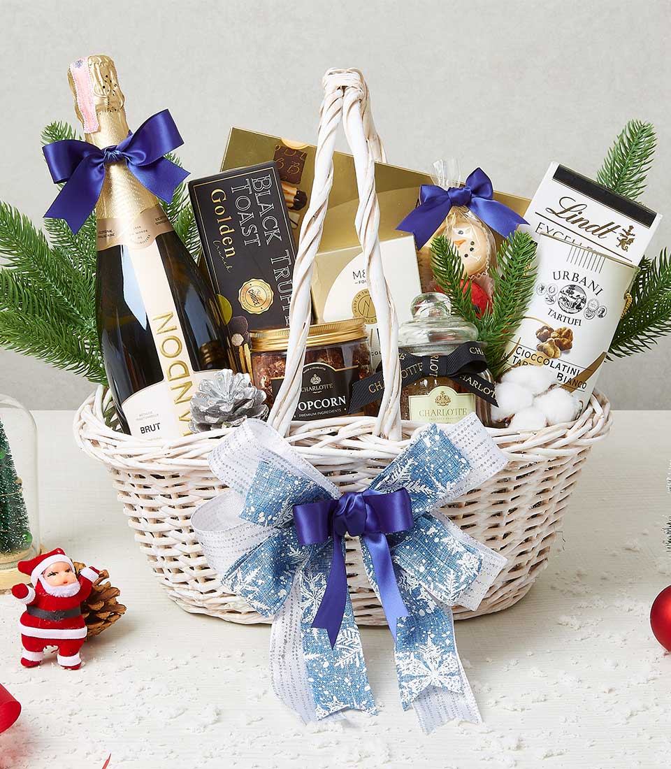 An elegant Basketeer gift basket brimming with a bottle of premium sparkling , gourmet chocolates, artisanal popcorn, and an assortment of delectable treats, all exquisitely adorned with luxurious ribbons and bows. The scene is beautifully enhanced with lush pine branches, festive holiday ornaments, including a charming Santa figurine. A Basketeer branded ribbon adds an extra touch of sophistication to this opulent festive presentation.