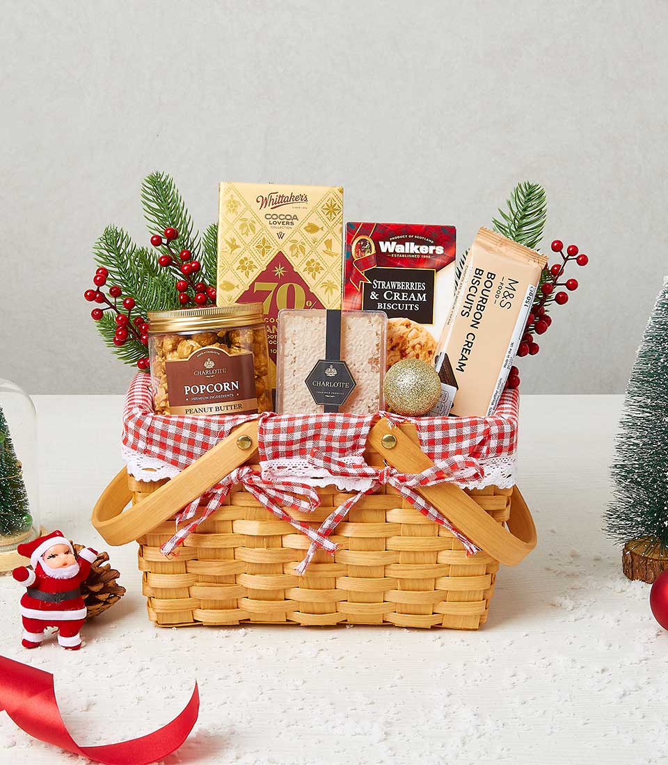 A luxurious wicker basket overflowing with gourmet holiday delights, featuring an exquisite jar of popcorn, a decadent box of chocolates, sumptuous Walkers shortbread, a rich Whitaker's chocolate bar, and a traditional Christmas pudding. This opulent arrangement is beautifully adorned with a red and white checkered cloth and elegant festive greenery. A ribbon exquisitely embossed with the Basketeer logo adds an extra touch of sophistication to this festive offering.