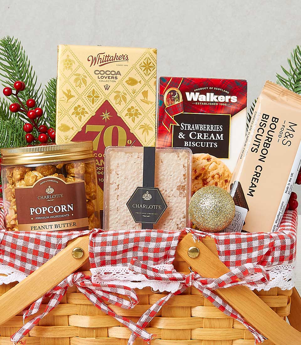 A luxurious holiday gift basket curated by Basketeer, brimming with an exquisite selection of premium treats. Inside, discover the rich decadence of Whittaker's 70% Cocoa chocolate and the delightful sweetness of Walker's Strawberries & Cream biscuits. Indulge in M&S Bourbon Cream biscuits and savor the gourmet experience of Charbonnel et Walker peanut butter popcorn, alongside buttery shortbread. The arrangement is elegantly adorned with festive greenery, nestled beautifully within a ribboned box proudly displaying the Basketeer logo for an inviting touch that elevates the gifting experience.