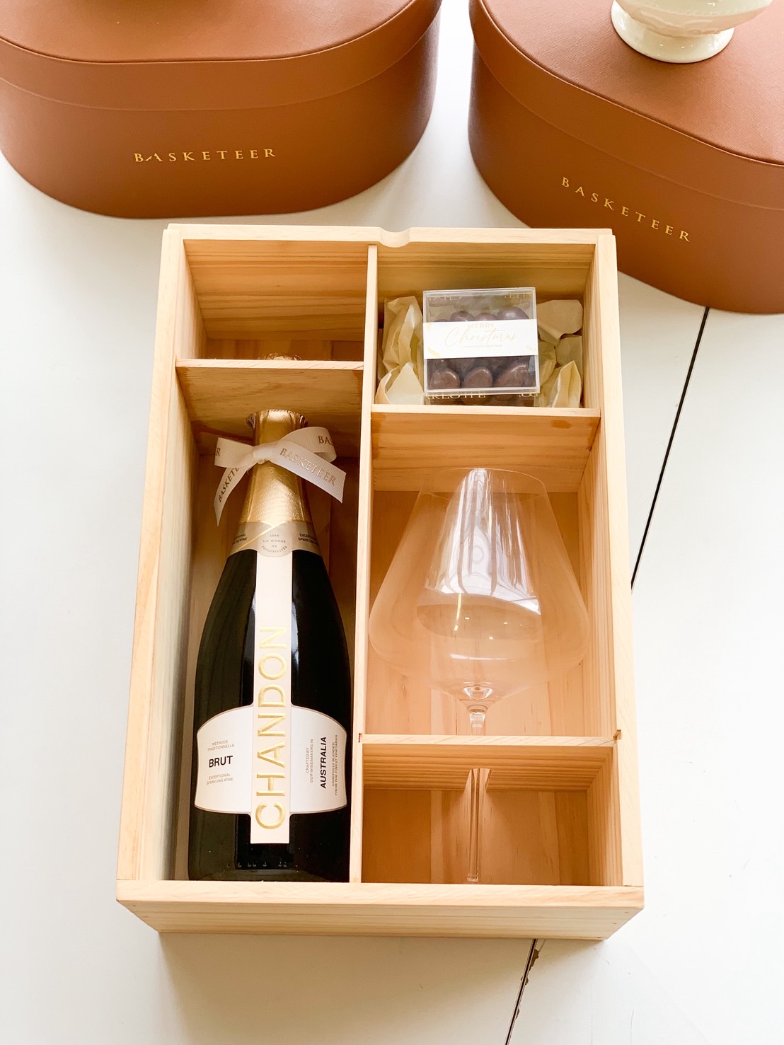 Wooden gift box featuring Chandon Brut sparkling wine, elegant wine glass, and chocolate gift pack