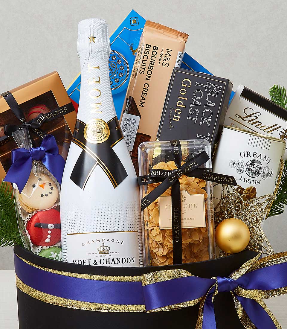 An opulent gift basket curated by Basketeer, featuring a prestigious bottle of Moët & Chandon champagne elegantly nestled among an exquisite selection of gourmet chocolates, a package of indulgent bourbon cream biscuits, and a box of sumptuous truffle crackers. The items are artfully arranged with luxurious festive ribbons and decorations, complemented by the distinguished Basketeer logo on the packaging, creating an inviting scene of refinement and celebration.