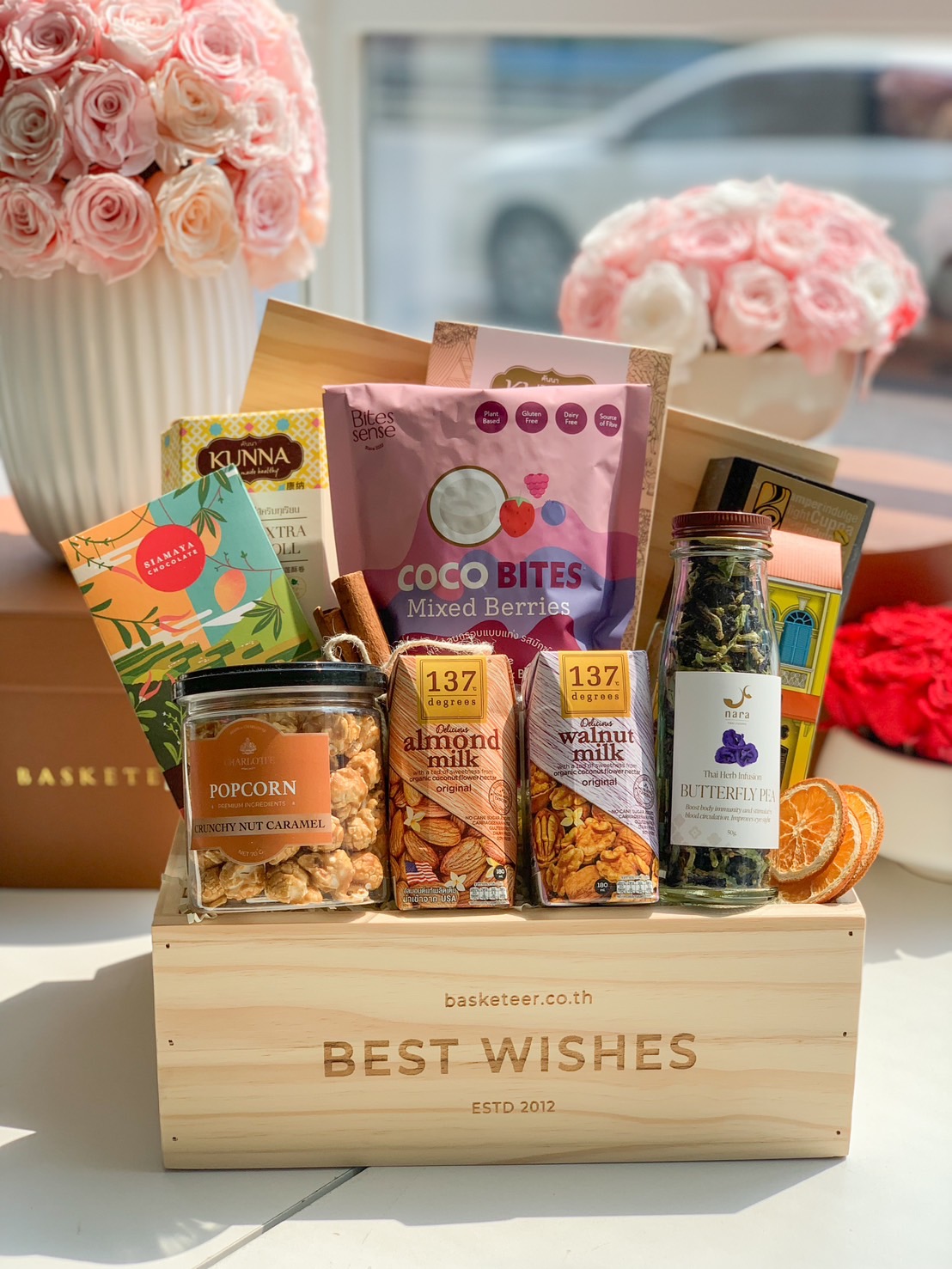 A luxurious wooden gourmet gift basket filled with healthy snacks, including almond milk, herbal tea, granola, dark chocolate, and caramel popcorn, elegantly packed with a 