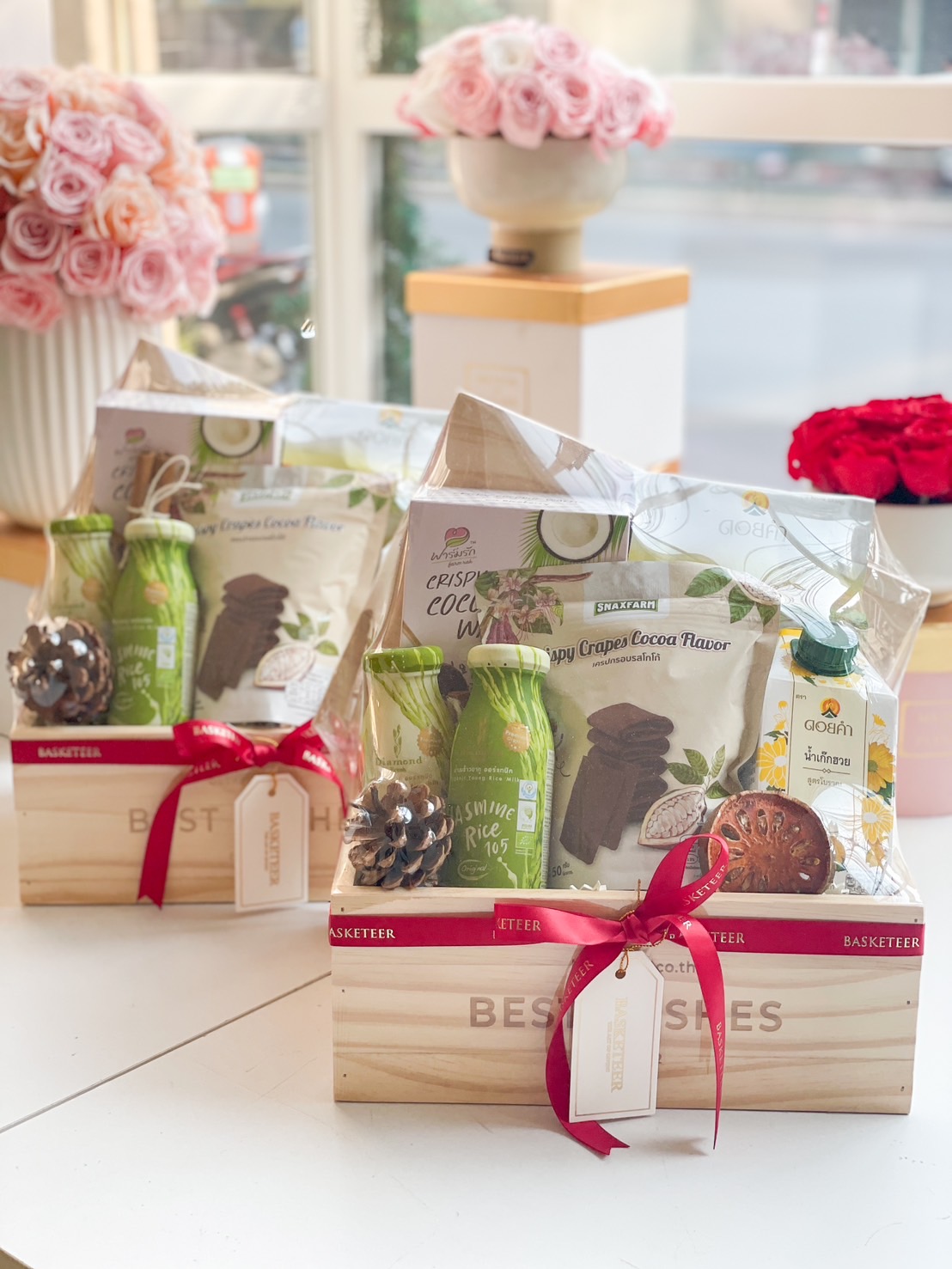 A beautifully packaged healthy Thai snack gift box, filled with organic coconut rolls, jasmine rice drinks, and herbal snacks, presented in a wooden crate with a festive ribbon.