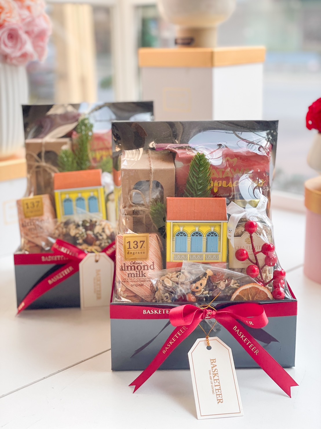 A beautifully designed luxury festive gift box, filled with premium almond milk, artisanal granola, dried fruit, and gourmet snacks, adorned with a red ribbon and elegant holiday decorations.