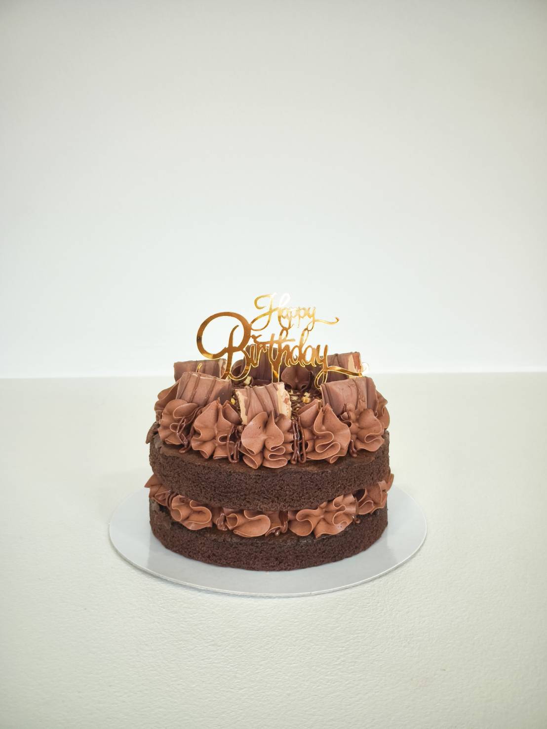 Two-layer chocolate birthday cake with ruffled chocolate buttercream and gold Happy Birthday topper