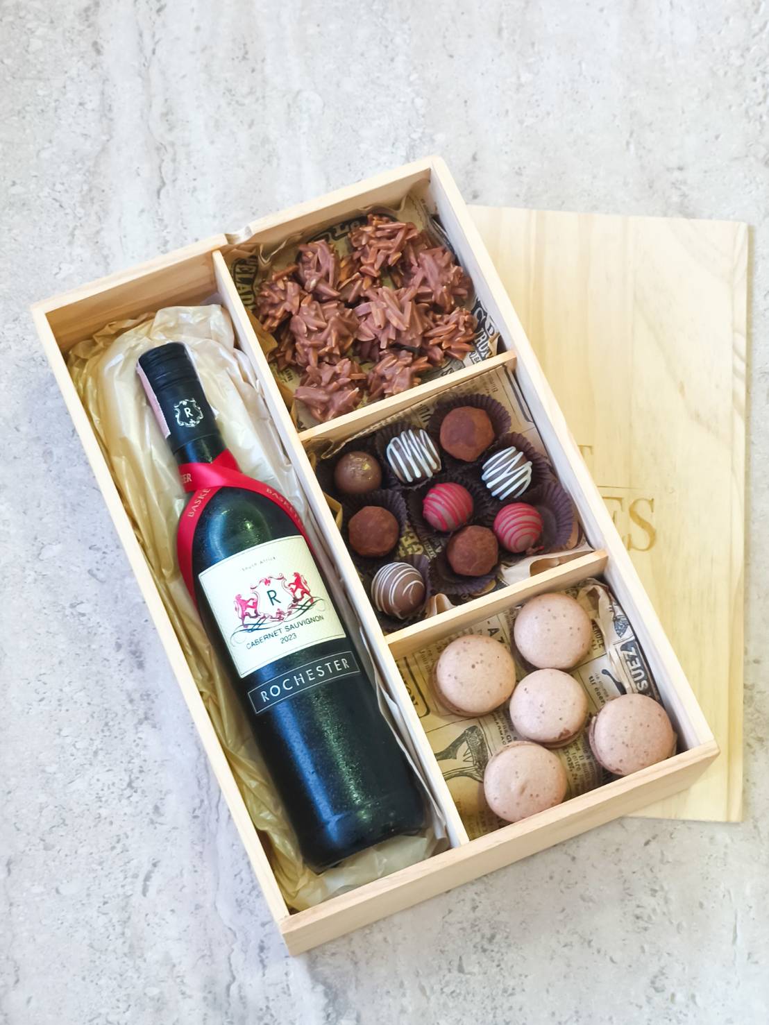 Luxury wine gift set with red wine, artisan chocolates, nut clusters, and macarons in a wooden box