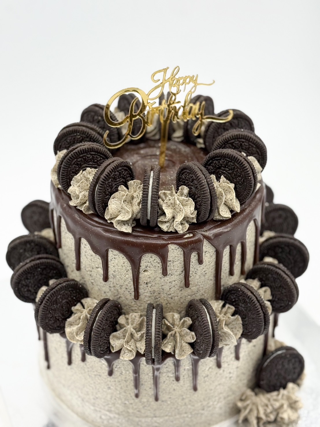 Close-up of a two-tier Oreo cookies and cream cake with rich chocolate ganache drips, topped and decorated with whole Oreos and swirls of cookies & cream frosting.