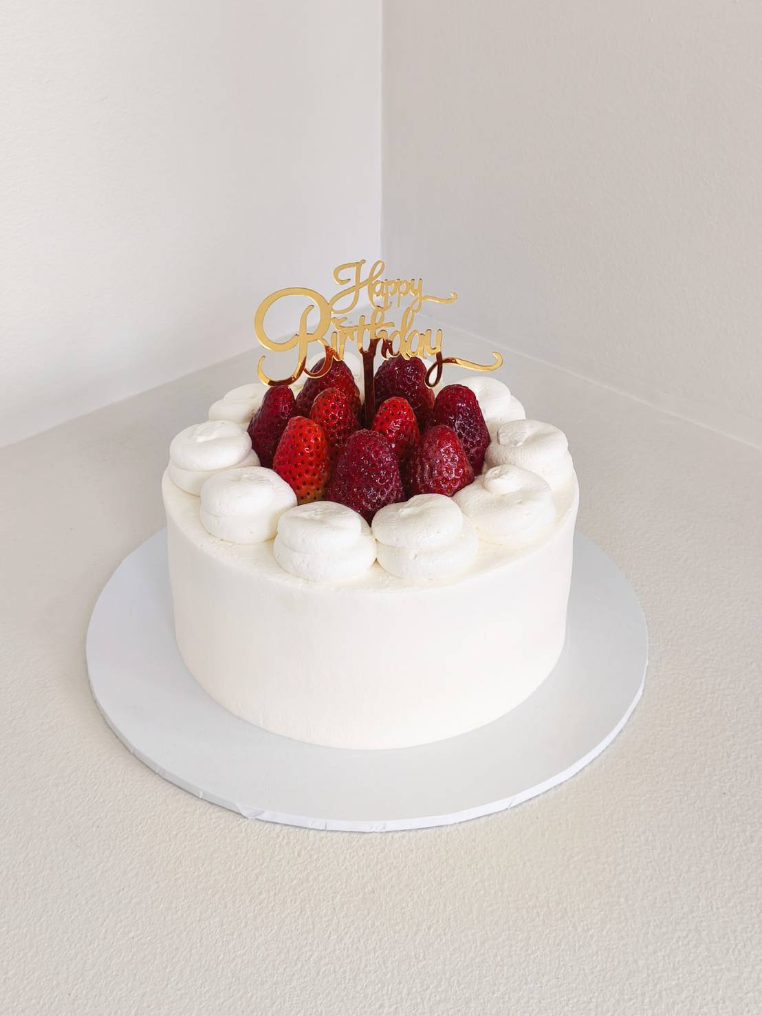 Fresh cream birthday cake topped with whole strawberries and whipped cream swirls, decorated with a golden 
