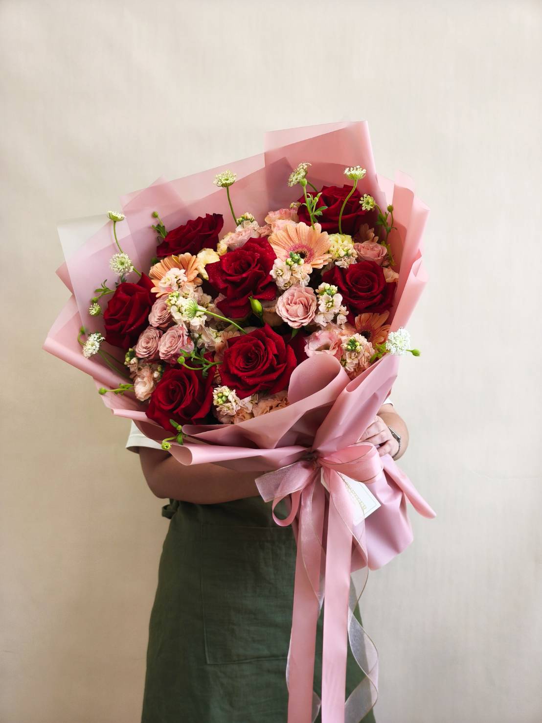 Romantic bouquet of red and peach roses, accented with delicate cream blooms, wrapped in pink paper with a satin ribbon.