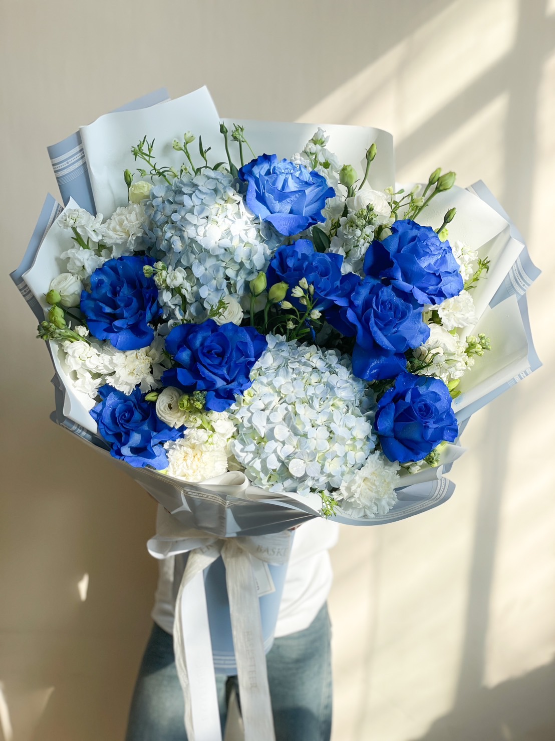 A breathtaking floral bouquet featuring vibrant royal blue roses, soft blue hydrangeas, and delicate white flowers, wrapped in an elegant pastel blue paper with a satin ribbon. A perfect choice for special occasions, luxury gifting, or romantic gestures.