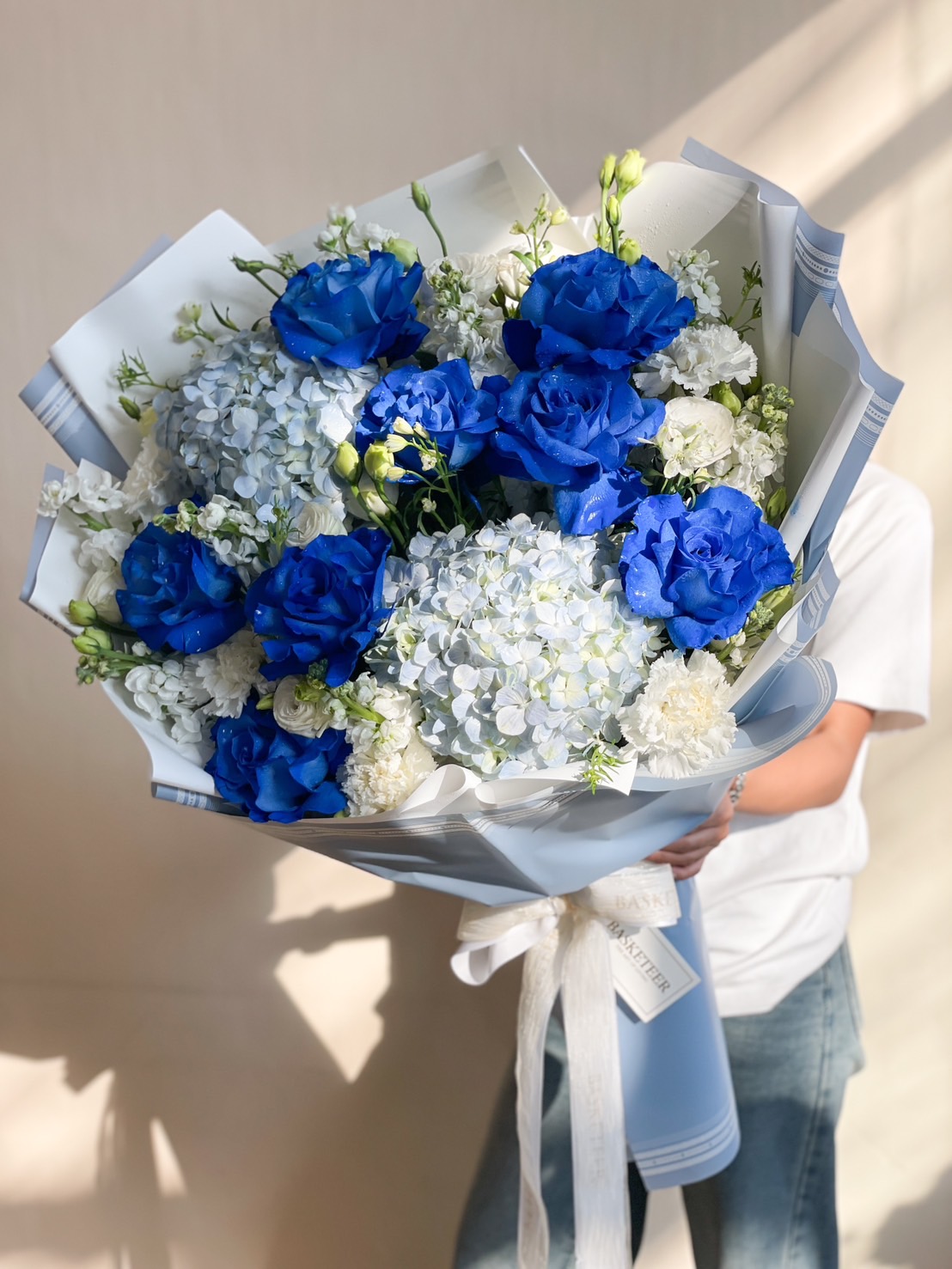 A breathtaking floral bouquet featuring vibrant royal blue roses, soft blue hydrangeas, and delicate white flowers, wrapped in an elegant pastel blue paper with a satin ribbon. A perfect choice for special occasions, luxury gifting, or romantic gestures.