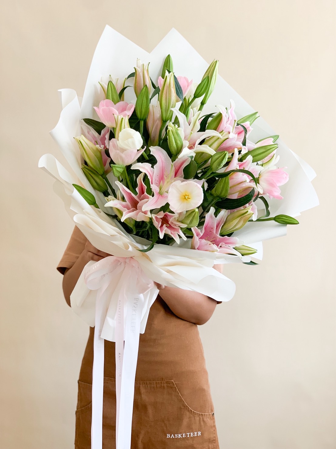 Large bouquet of pink stargazer lilies and white buds, wrapped in elegant white paper with long white ribbons.