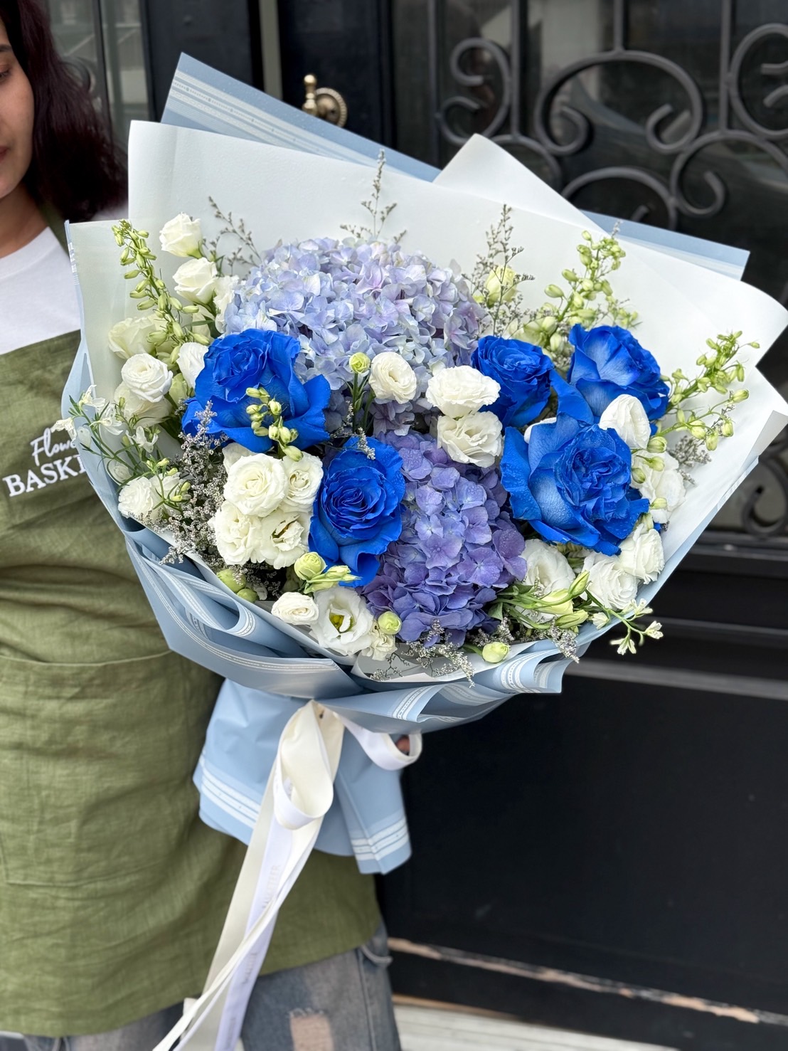 Hand-tied bouquet with blue roses, light and dark blue hydrangeas, and white lisianthus wrapped in blue-toned paper