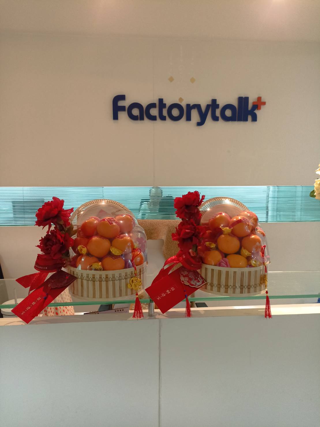 Two floral arrangements containing colorful fruits and adorned with red decorations are placed on a counter. In the background, a sign reads 