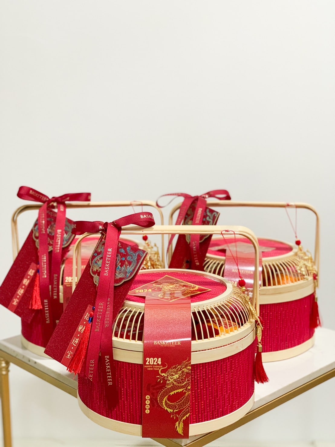 Three ornate red and gold lanterns with intricate designs are displayed on a surface. Each lantern is adorned with red ribbons and tassels featuring gold text and symbols, giving an elegant and festive appearance.