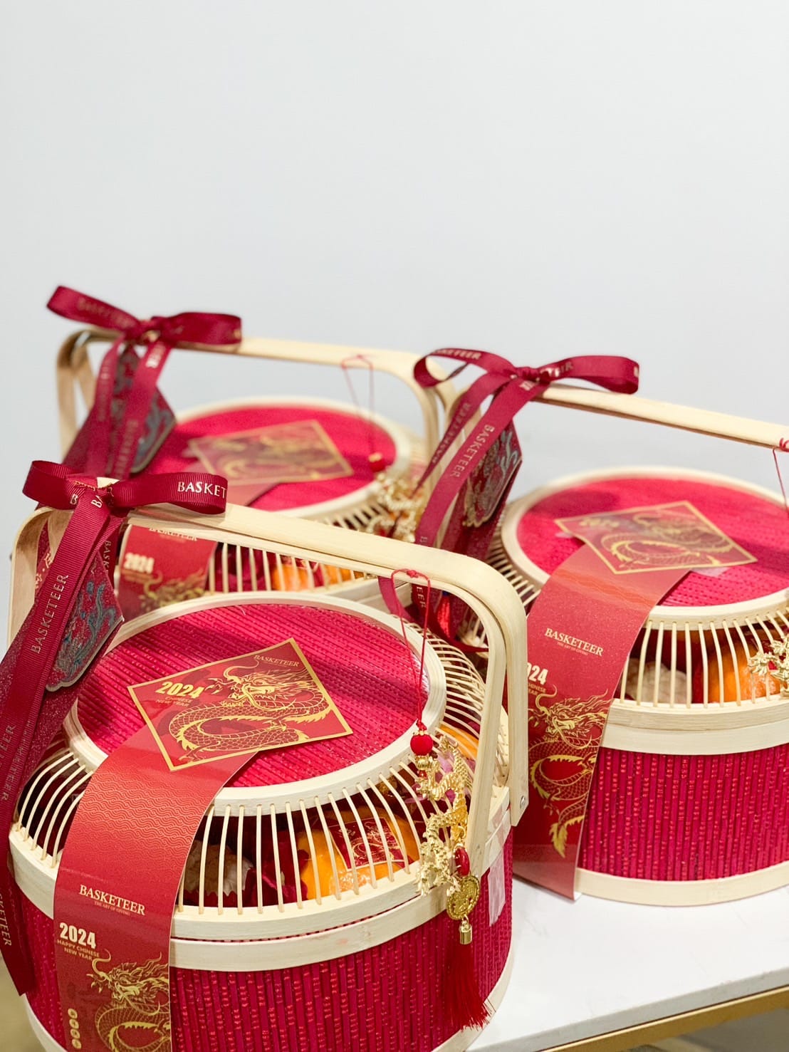 Four red and gold gift baskets with bamboo handles are decorated with intricate designs and red ribbons. The labels read 