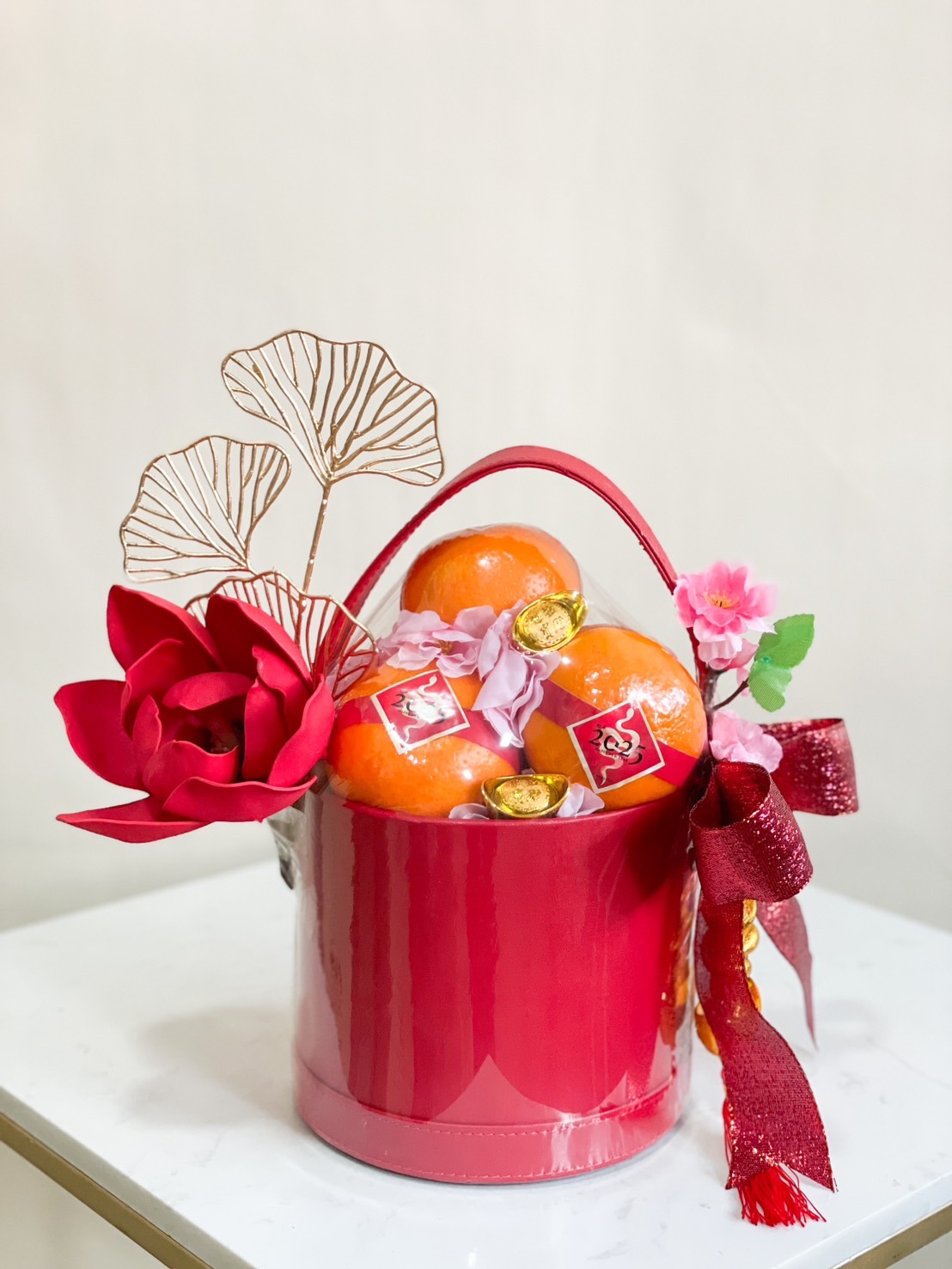 Red Lunar New Year gift basket filled with fresh mandarins, gold accents, floral decorations, and a festive red ribbon.