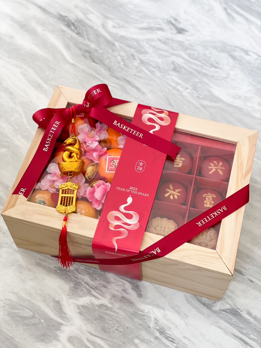 Elegant wooden gift box filled with Lunar New Year treats, mandarin oranges, and adorned with red Basketeer ribbons and a gold charm for the 2025 Year of the Snake.