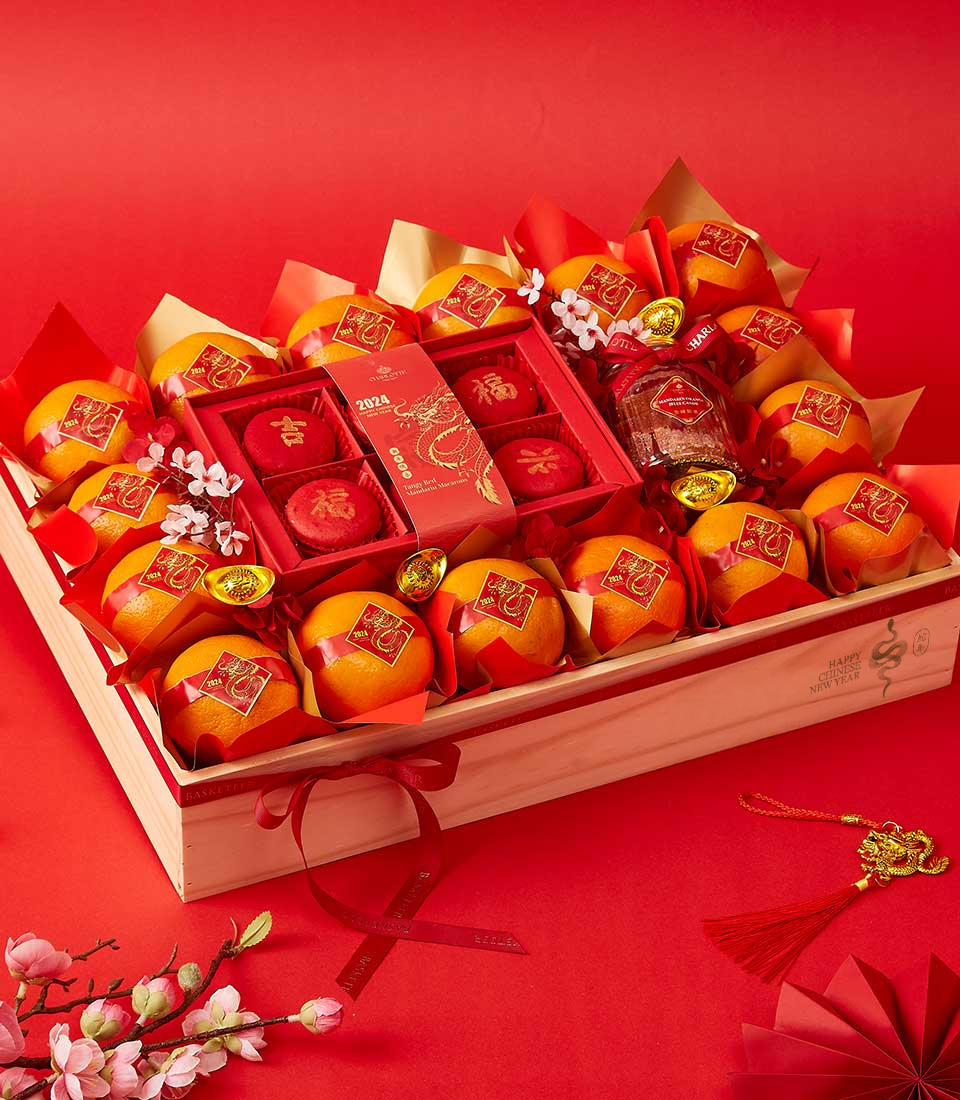 Mandarin oranges, red macarons with golden symbols, and festive decorations arranged in a luxurious wooden crate for Chinese New Year.
