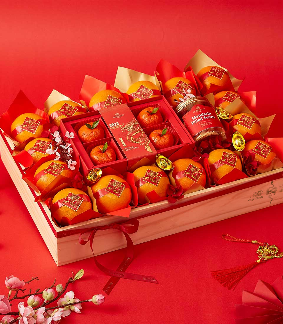 Chinese New Year gift hamper with mandarin oranges, red mooncakes, orange marmalade, and festive decorations in a wooden crate.