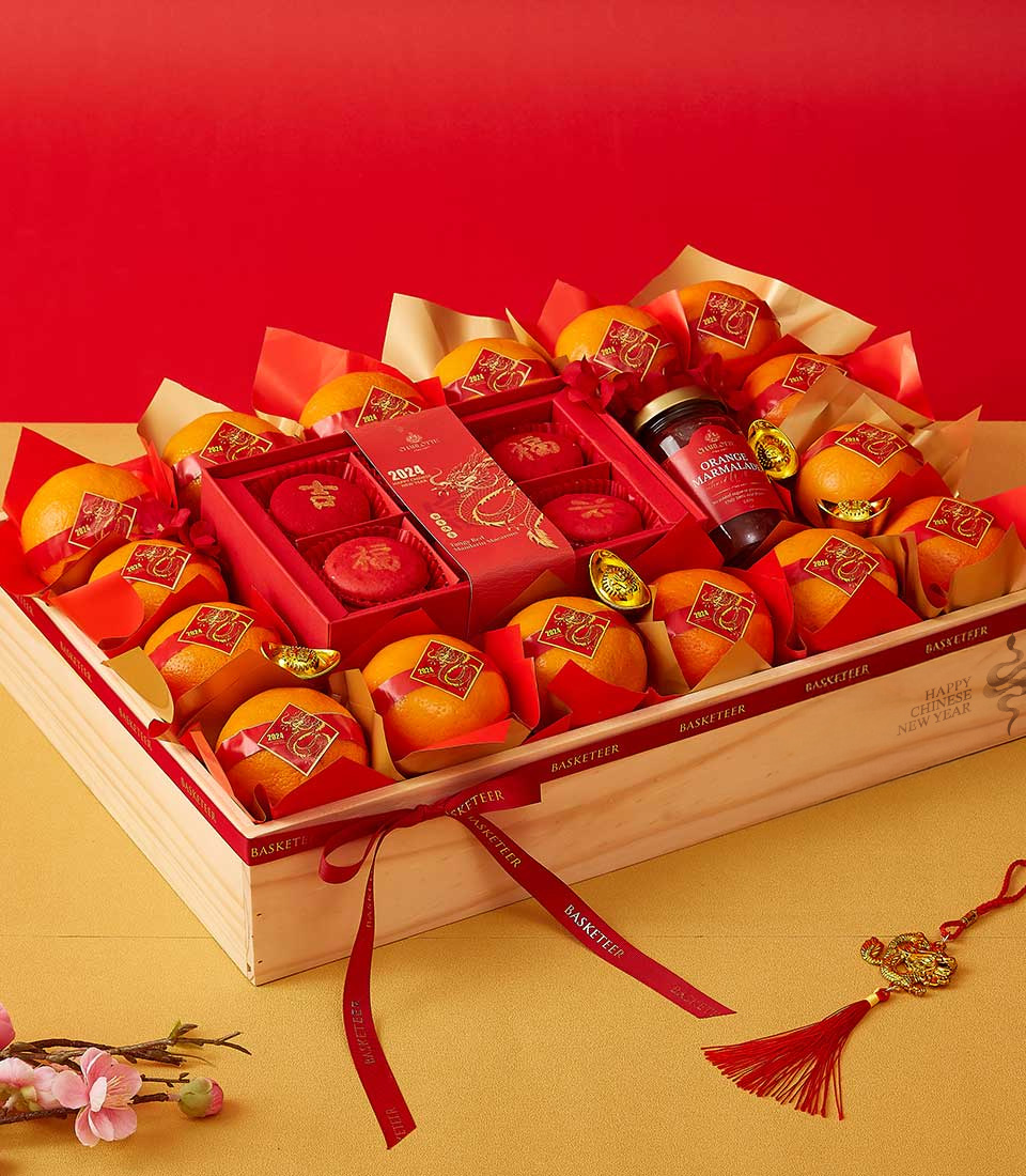 Chinese New Year gift hamper with mandarin oranges, red mooncakes, orange marmalade, and festive decorations in a wooden crate.