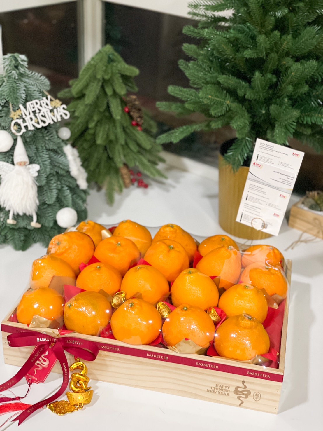 Wooden crate filled with premium mandarin oranges, adorned with red ribbons, gold ingots, and festive charms for Chinese New Year celebrations.