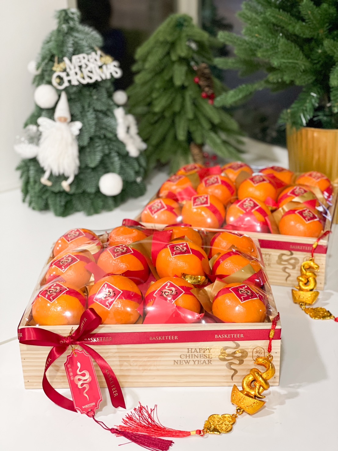 Wooden gift tray with fresh mandarin oranges, festive red ribbons, gold decorations, and 