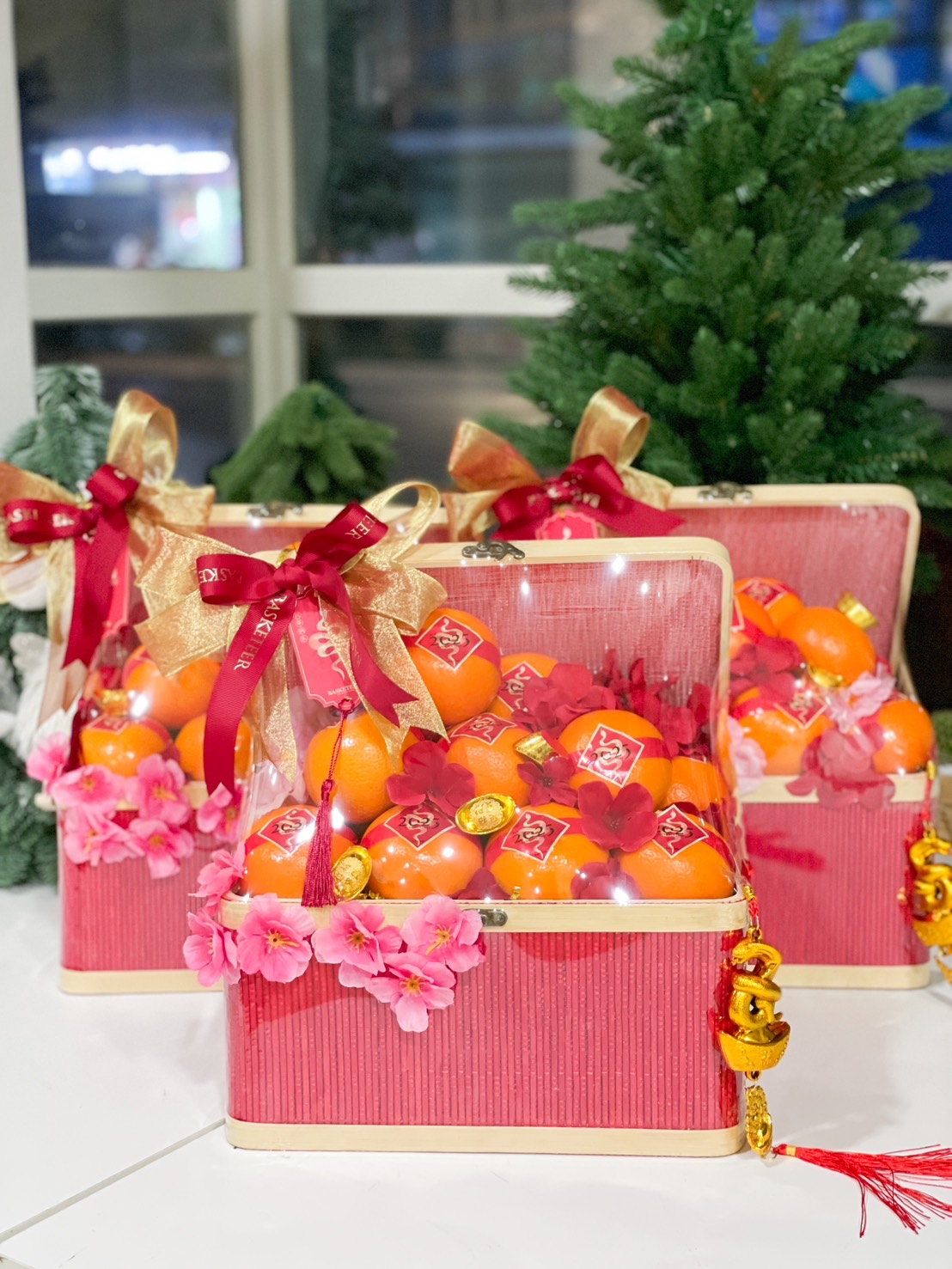 Mandarin orange gift basket with pink floral accents, golden coins, and red and gold ribbon, designed for Chinese New Year gifting.
