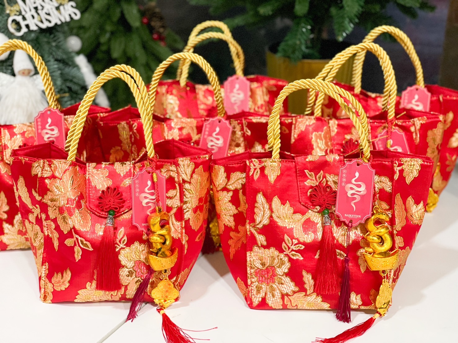 Chinese New Year festive tote bags in red and gold floral brocade, accented with gold rope handles, red tassels, and golden snake charms.