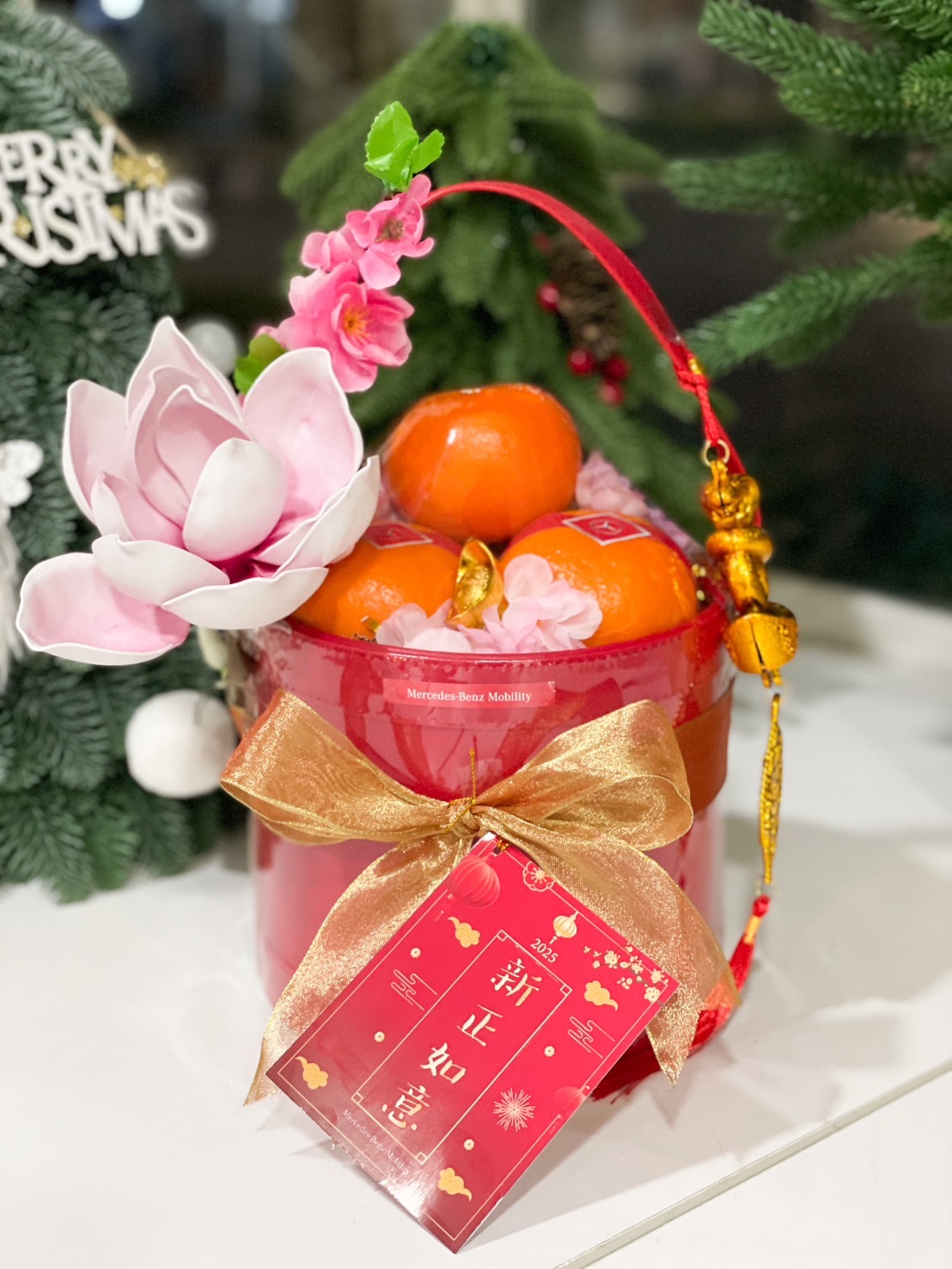 Red premium Chinese New Year gift basket featuring fresh oranges, pink decorative flowers, a golden bow, and festive gold accents, perfect for celebrations.