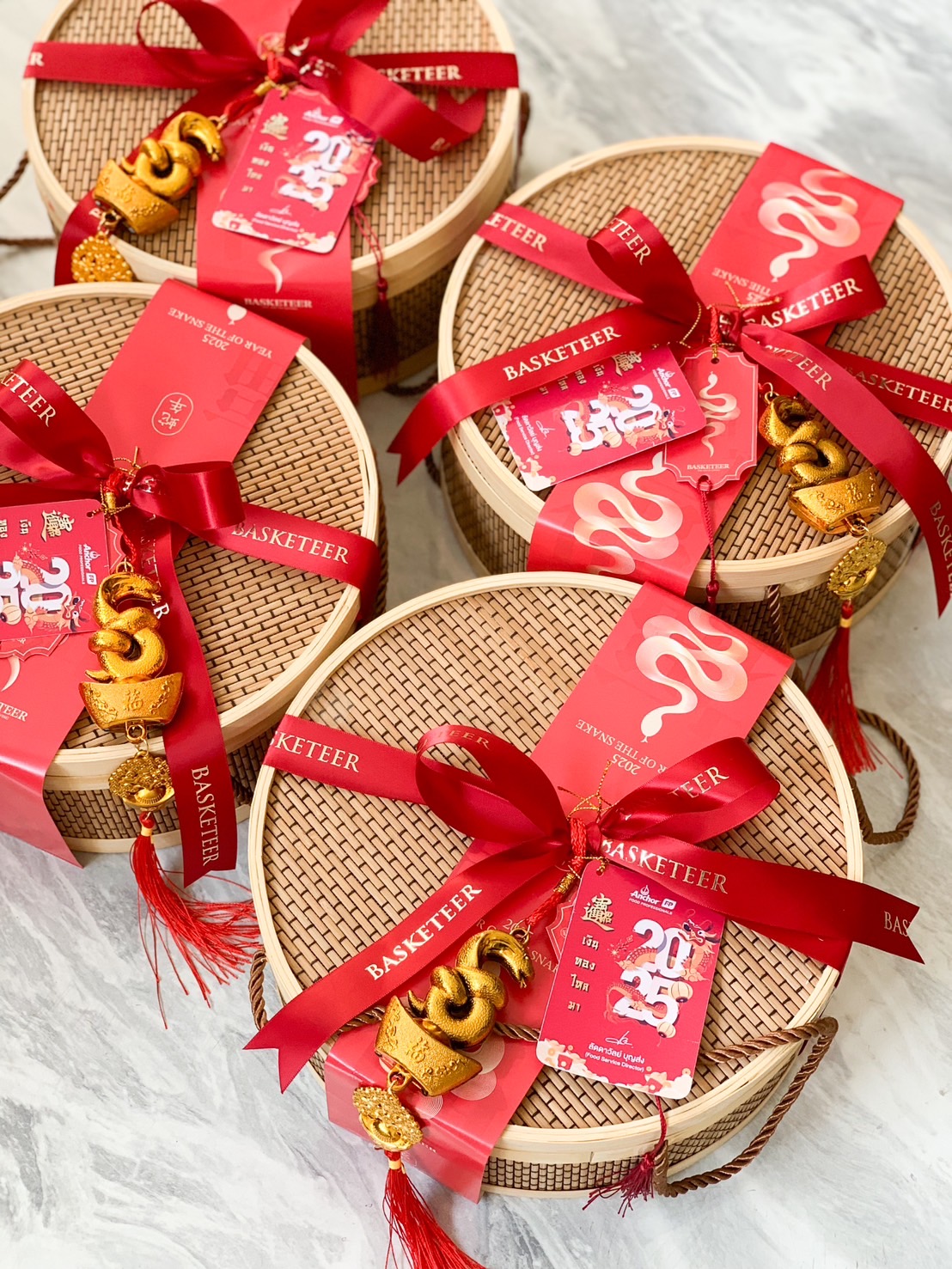 Close-up of a Chinese New Year bamboo gift baskets with red ribbons, festive gold charms, and traditional red packaging by Basketeer.