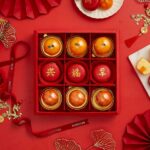 Chinese New Year Sweet Gift In Creamy Mandarin Center Cake, Mandarin Macarons, Salted Egg Cake In The Red Box With a Bow.