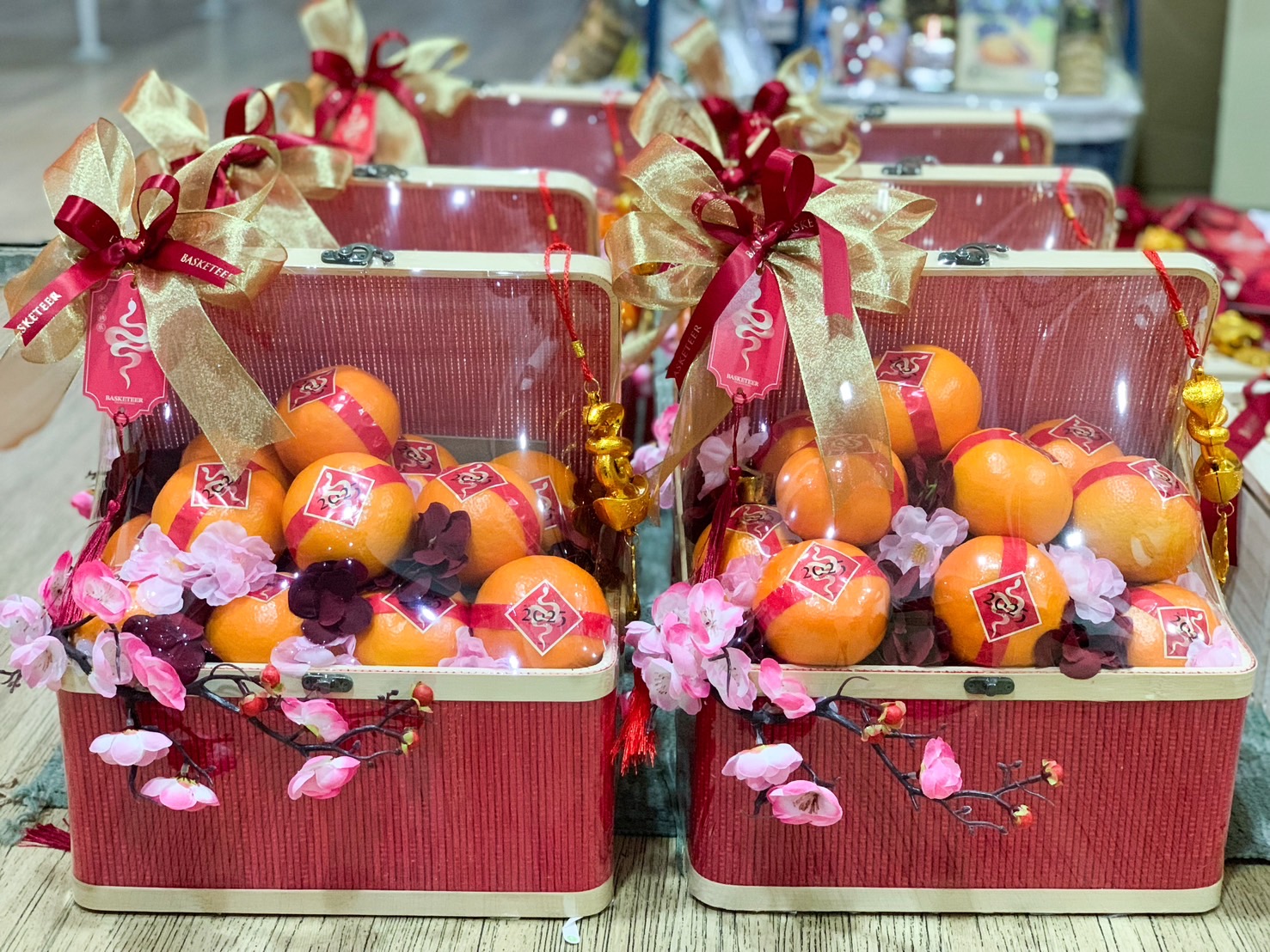 Chinese New Year treasure boxes filled with fresh mandarins, decorated with golden ribbons, pink flowers, and festive red tags.