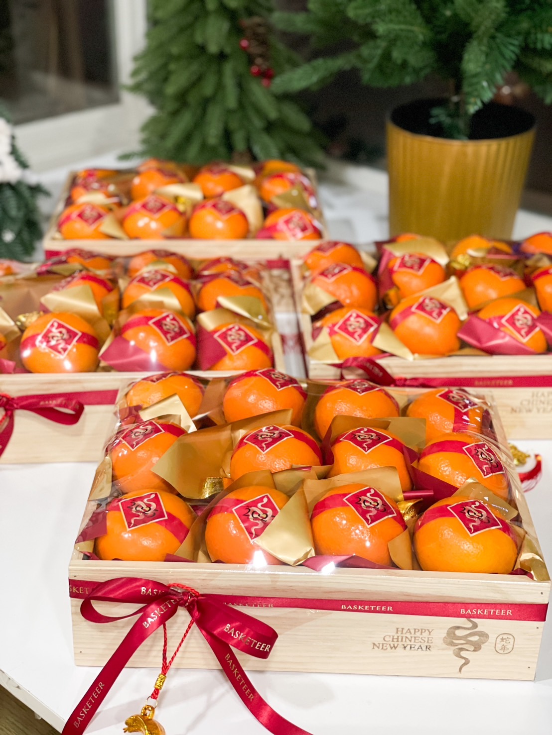 Wooden gift tray with fresh mandarin oranges, festive red ribbons, gold decorations, and 